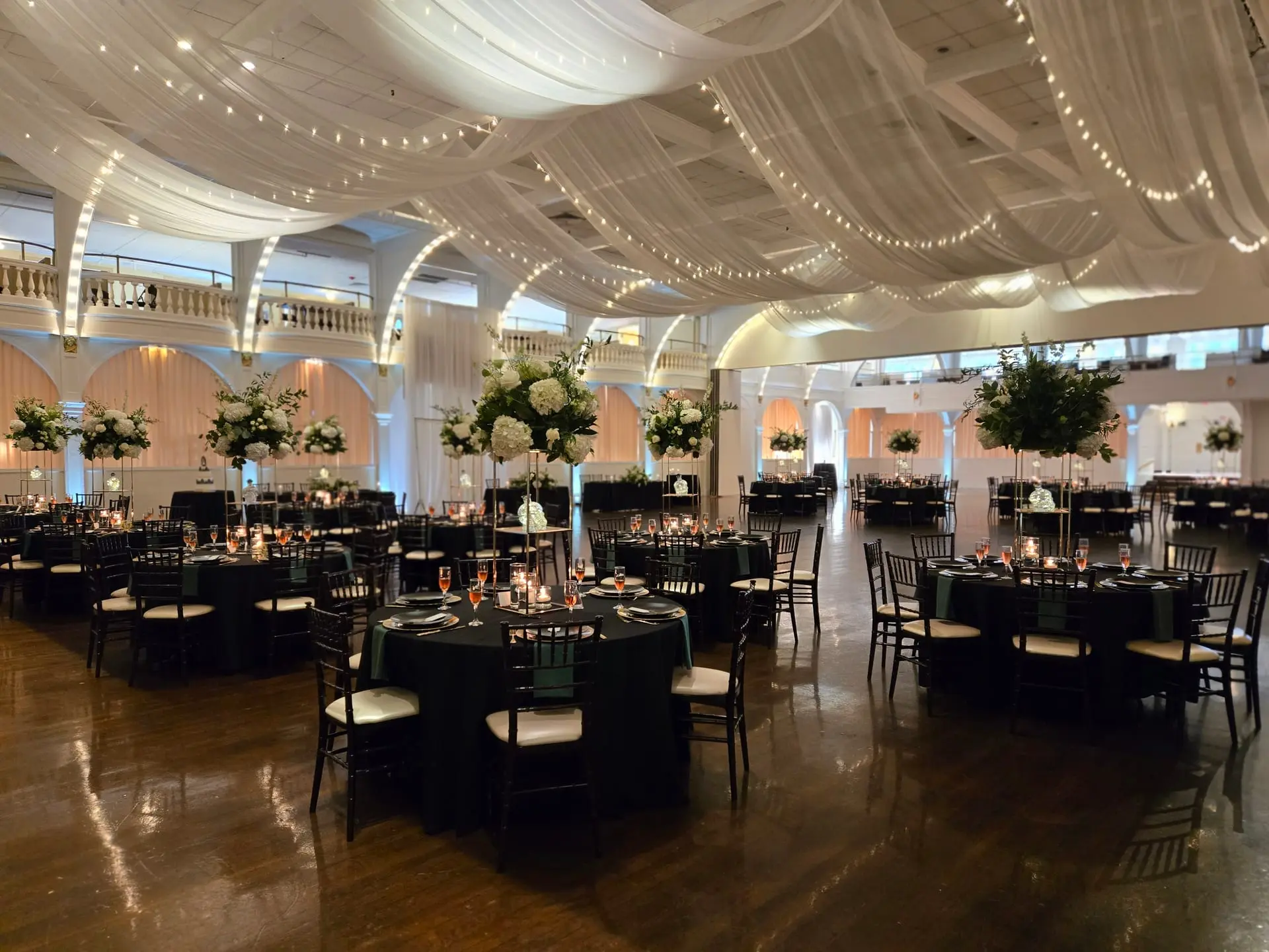 Ballroom set for a celebration, tables under warm uplighting and draped ceiling lights